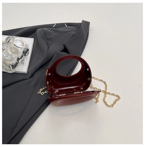 Borsa da sera circolare rosso scuro con catena in metallo dorato su sfondo chic