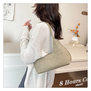 Detail of a beige knit underarm bag with a minimalist crescent shape on a model