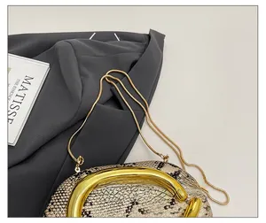 Detailed view of beige python skin evening clutch with bold gold metal handle and chain