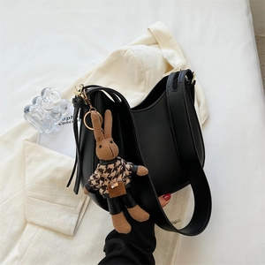 Chic black half-moon hobo bag with vintage knit bunny charm on an elegant suit