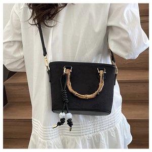 Detailed view of bamboo top handle and fringe tassel on black textured bucket bag