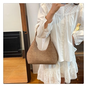 Brown woven crescent underarm bag shown with elegant white outfit in a home setting