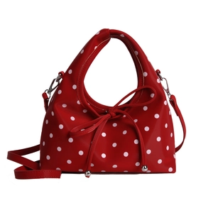Sac à bandoulière rouge à pois avec nœud et breloque sur fond blanc immaculé