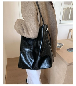 Close-up of black glossy crinkled leather tote bag worn by a model in a lifestyle setting