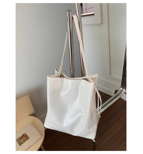 Detail of white high-gloss PU leather tote bag with drawstrings on a minimalist stand