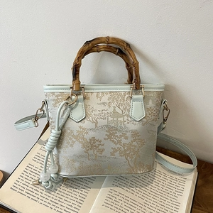 Light blue bucket bag with gold landscape print and bamboo handle on vintage books