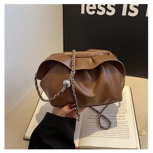 Brown pleated dumpling bag with silver chain and metal ball charm on book backdrop