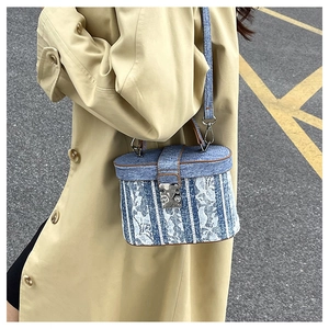 Dettaglio borsa a scatola in denim blu con motivi floreali in pizzo bianco e fibbia in metallo