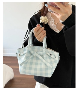 Détail du sac seau à carreaux bleu clair avec un grand nœud tenu par un mannequin