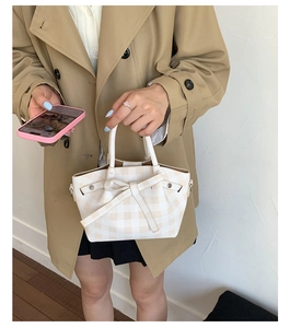 Détail d'un sac à main à carreaux avec grand nœud tenu par un mannequin en trench-coat