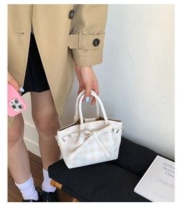 Détail du sac seau à carreaux avec nœud et anneaux sur le manteau du mannequin