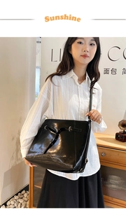 Detail of black glossy leather tote bag with decorative straps and metal buckles