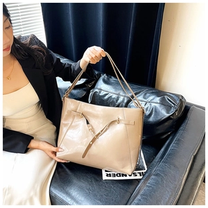 Detail view of glossy beige tote bag with slim straps and leather buckle accents