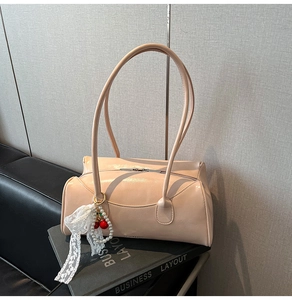Détail du sac beige verni avec nœud en dentelle et pendentif cerise sur des livres
