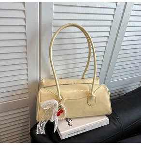 Détail d'un sac à main en cuir beige avec breloque cerise et nœud en dentelle