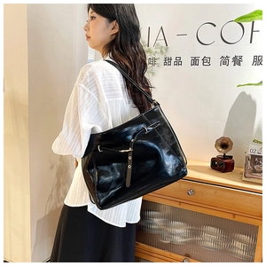 Detail of black glossy leather tote bag with gold buckle and strap on model in cafe