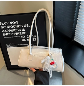 Détail du sac à main en cuir verni crème avec pendentif cerise et nœud en dentelle