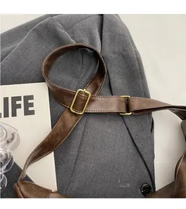 Detail of adjustable shoulder strap with gold buckle on a retro brown bucket bag