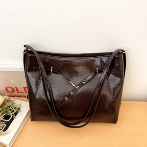 Detail of dark brown tote bag in oil wax leather finish with gold buckles on wooden desk