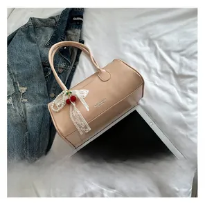 Détail du sac cylindrique en cuir rose avec breloque cerise et perle sur lit blanc