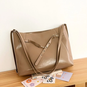 Close-up of khaki leather tote bag with decorative buckle straps on a wooden surface