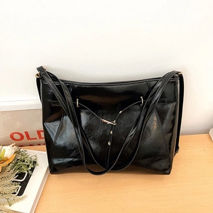 Glossy black patent leather tote bag with gold metal buckle on light wooden table