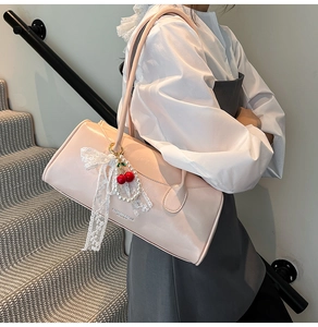 Détail du sac à main en cuir rose avec nœud en dentelle blanche et pendentif cerise