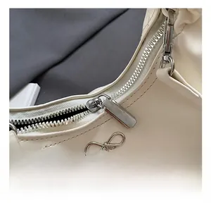 Détail de la fermeture éclair argentée et du nœud métallique sur le sac à main blanc crème