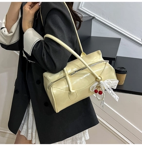 Détail d'un sac cylindrique jaune verni avec nœud en dentelle et pendentif cerise perlé