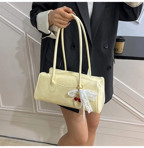 Détail du sac cylindrique crème avec nœud en dentelle et pendentif cerise