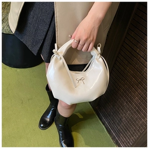 Détail du sac demi-lune crème avec fermoir nœud doré porté dans un cadre lifestyle