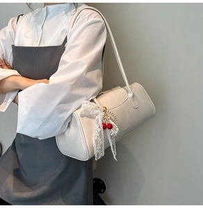 Détail du sac polochon blanc crème avec nœud en dentelle, breloque cerise et perles