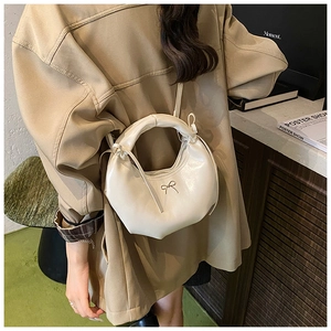 Détail du sac hobo en cuir blanc crème avec nœud métallique porté avec un manteau kaki