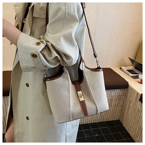 Close-up of canvas and leather bucket bag featuring a gold twist lock and fine strap