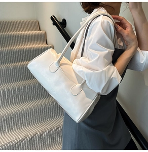 Détail d'un sac à main en cuir blanc avec bandoulière porté devant un escalier épuré