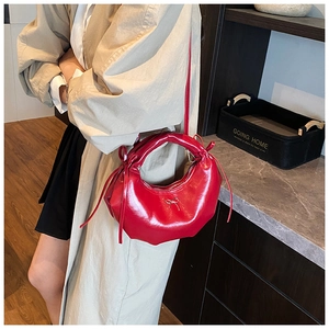 Détail du sac hobo en cuir verni rouge avec nœud en métal et pompons latéraux