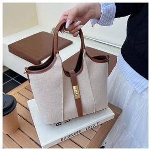 Detail of canvas tote bag with brown leather trim and golden twist lock on wooden desk