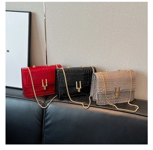 Three flap square bags with crocodile pattern and golden chain on a leather bench