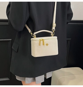 Detail of a cream leather mini box bag with golden hardware and camellia flower ornament