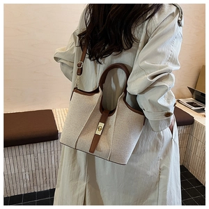 Detail of canvas and leather tote with gold twist-lock closure on light beige trench coat