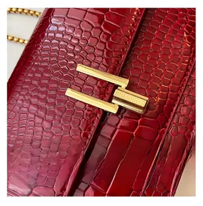 Close-up of deep red crocodile embossed leather handbag with gold geometric metal clasp