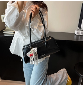 Détail du sac à main en cuir noir avec lettrage blanc et breloque cerise et perles