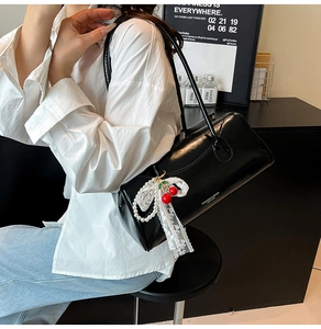 Détail d'un sac cylindrique noir avec pendentif cerise et nœud en dentelle blanche