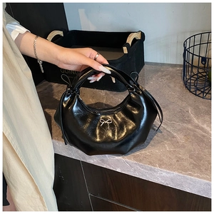 Détail du sac croissant noir brillant avec nœud argenté et texture plissée élégante