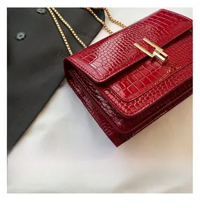 Close-up of red crocodile-embossed leather texture with golden metal chain and geometric lock