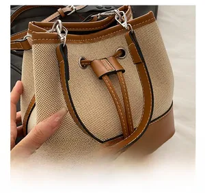Detail showing the beige canvas fabric and brown leather trim of the bucket handbag