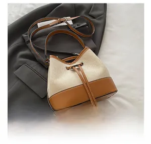 Detail of drawstring bucket bag featuring beige canvas and brown leather contrast stitching