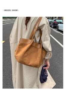 Close-up of a large brown suede tote bag with leather trim detail shown in a street scene