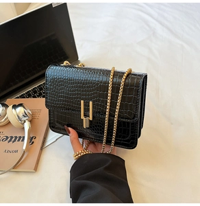 Close-up of black crocodile pattern leather bag with golden chain and metal lock detail