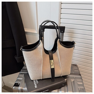 Detailed shot of beige canvas tote with black leather trim and gold metal twist lock